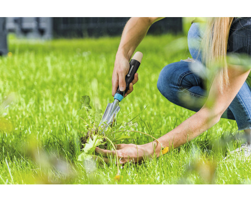 Eine Person entfernt Unkraut mit einer Gartenschaufel von Gardena aus dem Rasen.