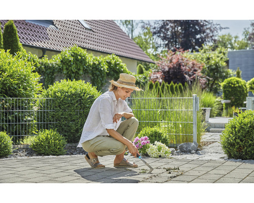 Une femme enlève les mauvaises herbes avec un désherbeur de joints sur une terrasse pavée.