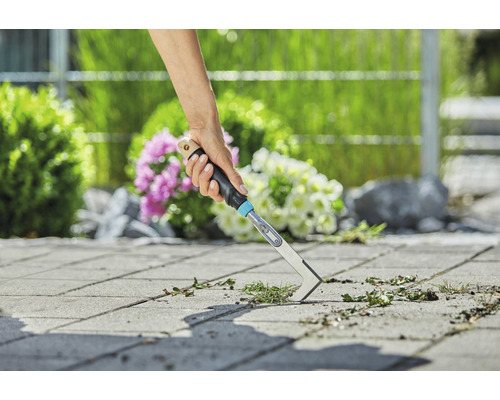 Une personne enlève les mauvaises herbes des pavés d''un jardin avec un désherbeur de joints.
