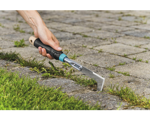 Une personne enlève les mauvaises herbes entre les pavés avec un désherbeur de joints.