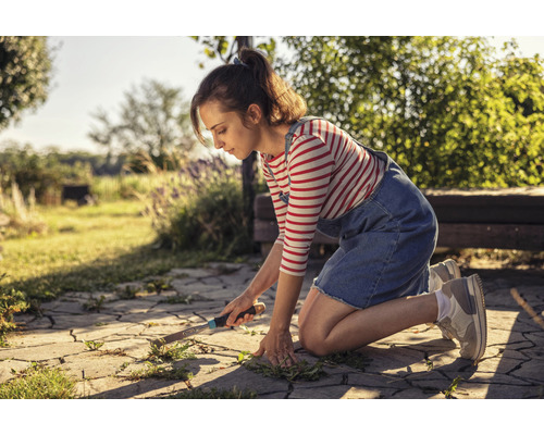 Une femme retire les mauvaises herbes des pavés de son jardin à l''aide d''un couteau à désherber.