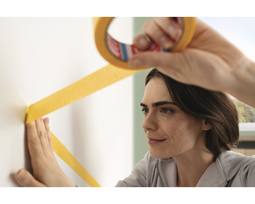 Frau bringt Malerband an der Wand an