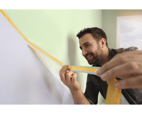 Ein Mann verwendet Malerkrepp, um eine Wand für Malerarbeiten vorzubereiten.