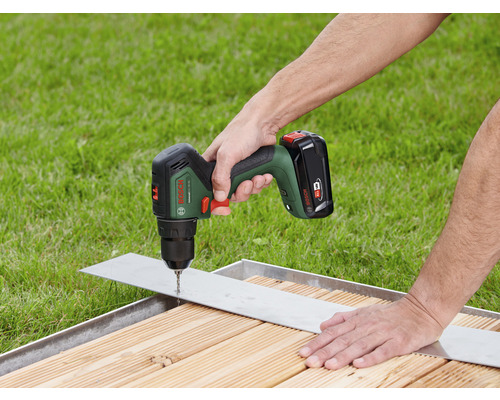 Tournevis sans fil perçant un trou dans une pièce métallique sur une surface en bois.