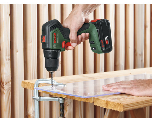 Une personne perce une plaque de plastique avec une perceuse-visseuse sans fil Bosch, fixée à une surface en bois avec un serre-joint.