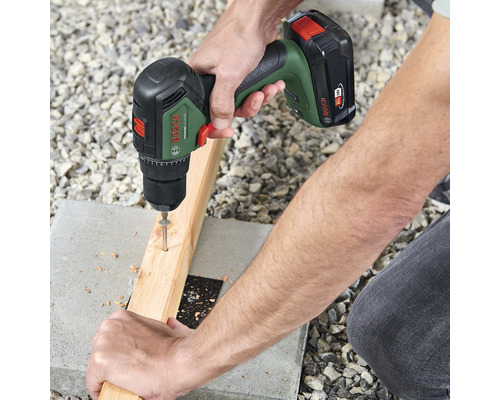 Une personne visse une vis dans une planche de bois à l'aide d'une perceuse-visseuse sans fil