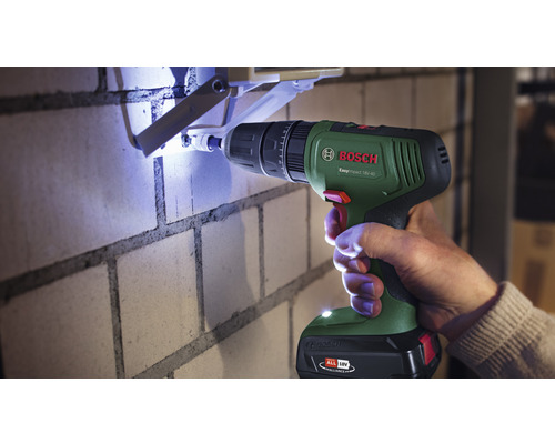 Une personne perce un trou dans un mur de briques avec une perceuse à percussion sans fil Bosch.