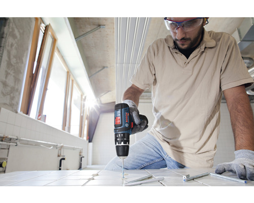 Un artisan perce des trous dans des carreaux avec une perceuse sans fil.