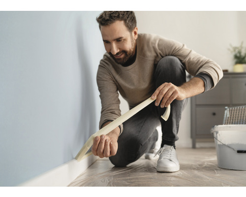 Ein Mann klebt Malerkrepp an eine Wand in einem Raum.