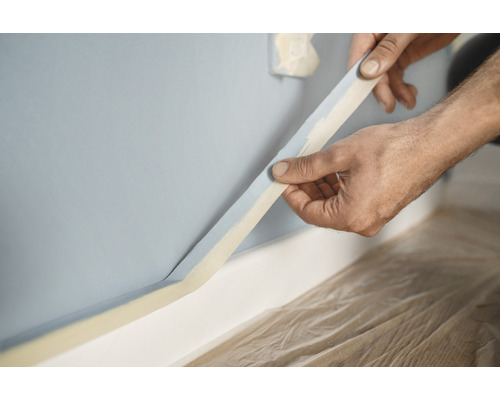 Eine Person klebt Malerkrepp an eine Wand zur Vorbereitung von Malerarbeiten.