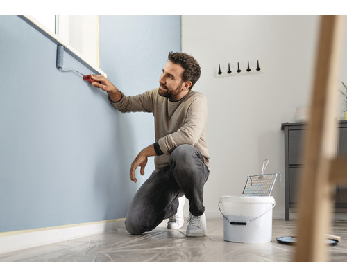 Mann streicht Wand mit Farbroller in einem Raum