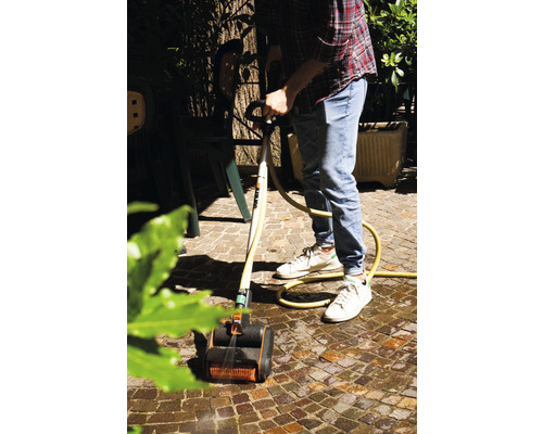 Un homme nettoie des pavés avec une brosse de nettoyage et un tuyau d''arrosage dans le jardin.