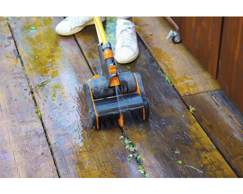 Une personne nettoie une terrasse en bois avec une brosse et de l''eau.