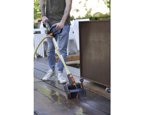 Une personne nettoie une terrasse en bois avec un nettoyeur de terrasse de Worx.