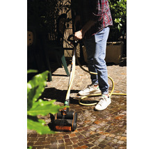 Un homme nettoie des pavés avec un nettoyeur de terrasse et un tuyau d''arrosage dans le jardin