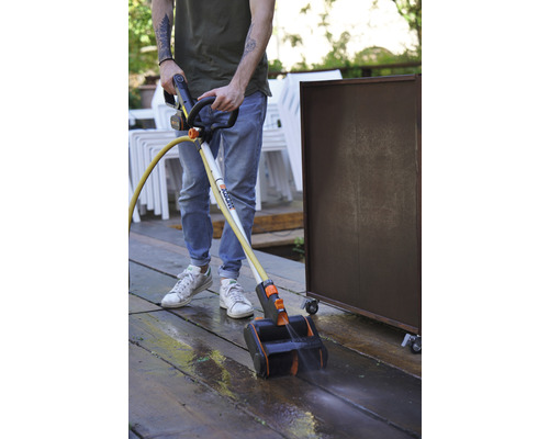 Une personne utilise un nettoyeur de terrasse pour nettoyer une terrasse en bois.