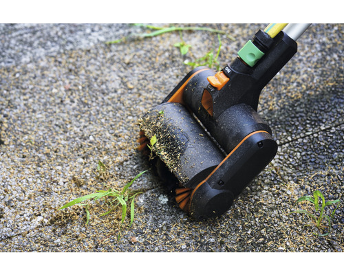 Fugenbürste in Aktion beim Entfernen von Unkraut auf einer gepflasterten Fläche.