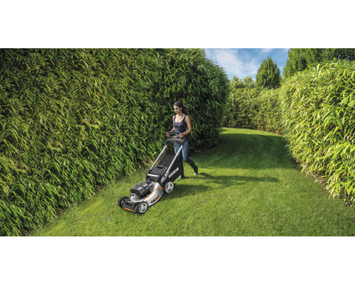 Eine Frau mäht den Rasen mit einem Rasenmäher in einem Garten mit Bambushecken.