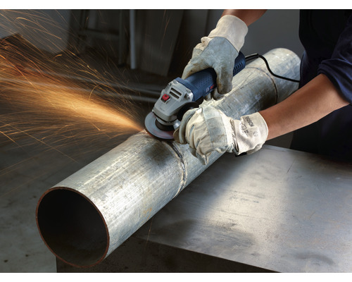 Eine Person benutzt eine Schleifmaschine an einem Rohr, Funken fliegen.