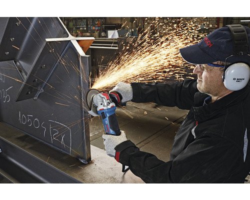 Un ouvrier utilise une meuleuse d''angle sur une pièce métallique, produisant des étincelles. L''ouvrier porte des équipements de protection, notamment une protection auditive.