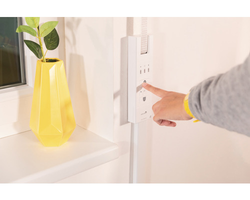 Person bedient einen Rollladen-Zeitschaltuhr neben einer Dekoration auf einer Fensterbank