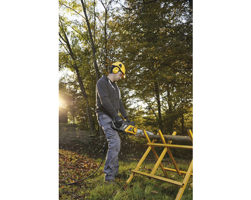 Un homme scie une bûche avec une tronçonneuse électrique sur un chevalet dans le jardin.
