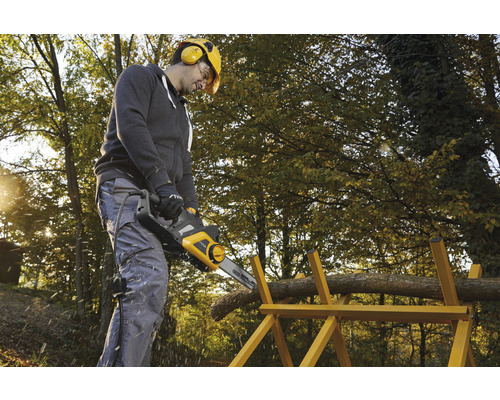 Un homme scie du bois avec une tronçonneuse électrique sur un chevalet à l''extérieur.