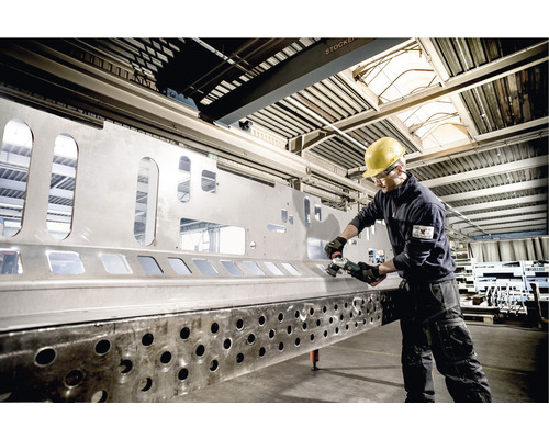 Ein Arbeiter bearbeitet eine große Metallplatte mit einem Winkelschleifer in einer Werkshalle.