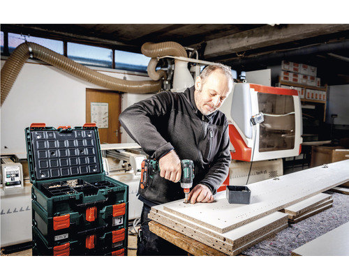 Handwerker arbeitet mit einem Akkuschrauber an einem Werkstück, im Hintergrund eine Werkzeugkiste