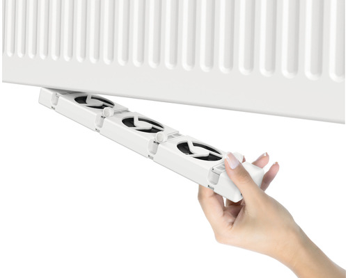 Une personne installe un ventilateur de radiateur sous un radiateur