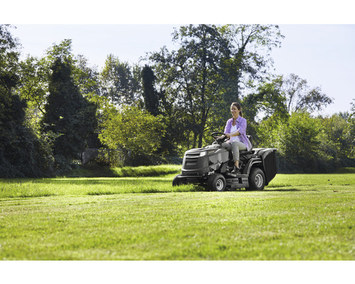 Une femme conduit un tracteur de pelouse sur une pelouse.