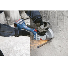 Eine Person schneidet mit einem Akku-Winkelschleifer ein Metallteil an einer Wand.