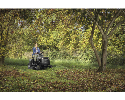 Femme conduisant une tondeuse autoportée dans un jardin avec des arbres.