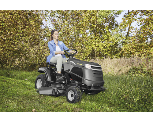 Femme conduisant un tracteur de jardin sur une pelouse avec des arbres en arrière-plan