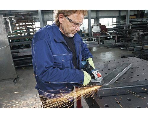Ein Mann schleift Metall mit einem Winkelschleifer in einer Werkstatt.