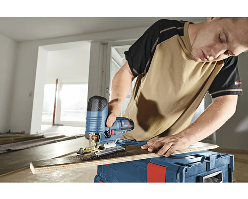 Un homme coupe une planche avec une scie sauteuse sur une caisse à outils.