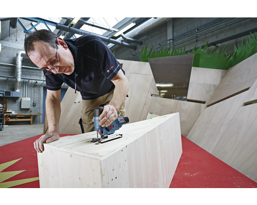 Un homme scie du bois avec une scie sauteuse. La scie sauteuse est de Bosch.