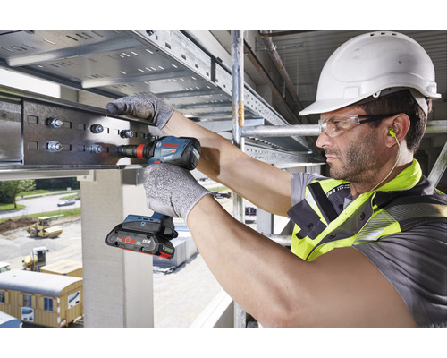 Ein Bauarbeiter befestigt mit einem Akku-Schlagschrauber eine Metallschiene.