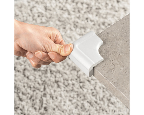 Une main fixe une protection d''angle blanche sur un bord de table.
