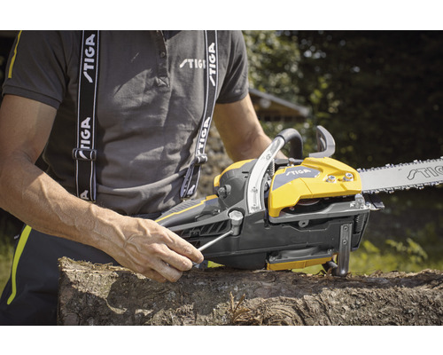 Une tronçonneuse jaune et grise est ajustée par une personne avec une clé sur une bûche.