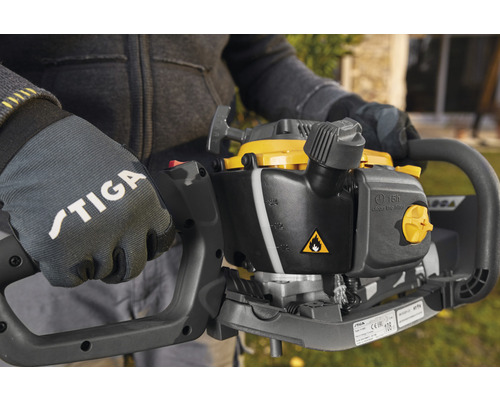 Nahaufnahme einer Person mit Stiga-Handschuhen, die eine Heckenschere hält.