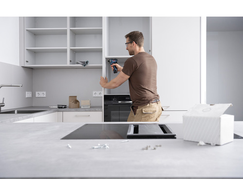 Un homme installe une cuisine équipée avec un tournevis sans fil dans une cuisine claire.