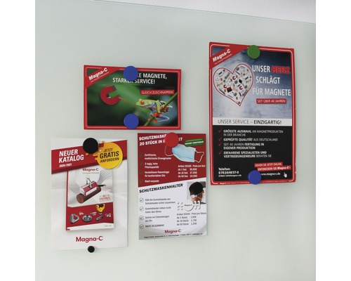 An einer Wand hängen vier Werbebroschüren mit Magneten der Marke Magna-C. Sie bewerben Magnete, Schutzmasken und Kataloge.