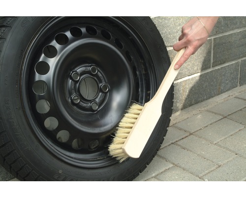 Stahlfelge mit Winterreifen wird mit einer Bürste gereinigt.