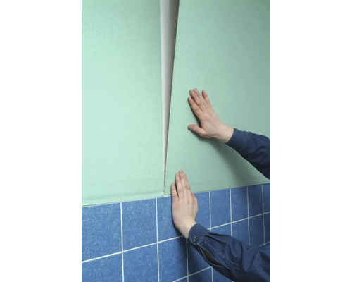 Person befestigt eine Gipskartonplatte an einer Wand über Fliesen.