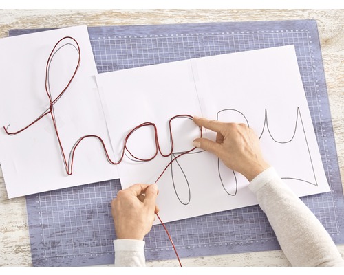 Frau formt mit Draht das Wort Happy auf Papier