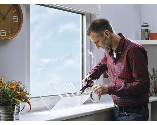 Mann schneidet mit einer Schere ein Insektenschutzgitter am Fenster zu.