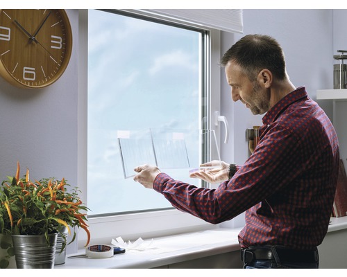 Mann befestigt eine transparente Folie an einem Fenster.