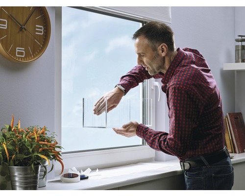 Mann befestigt Isolierfolie an einem Fenster zur Wärmedämmung.