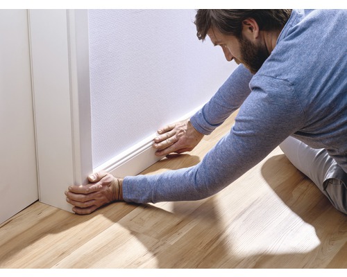 Mann montiert Sockelleiste an einer Wand
